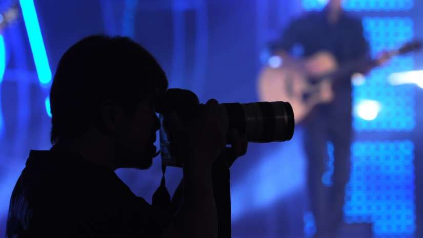 En eventfotograf i silhuett fotograferar en konsert med blått scenljus.