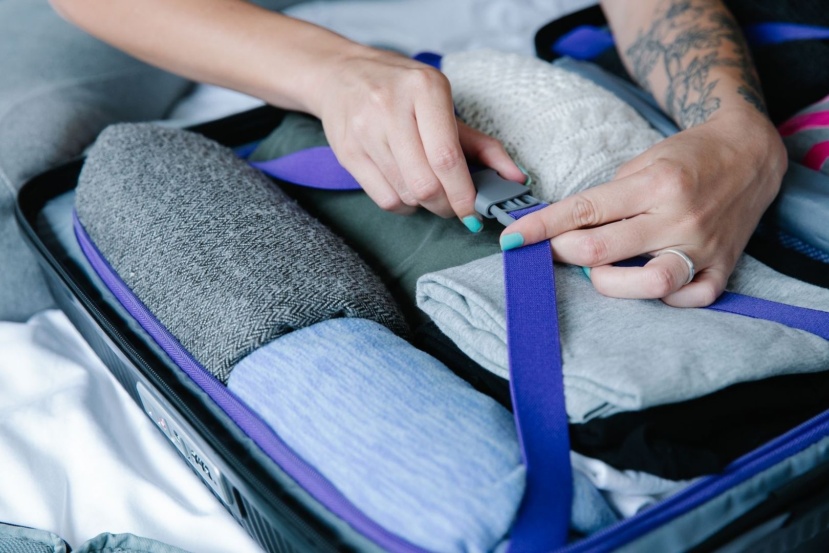 Händer spänner ett packband över prydligt vikta kläder i resväska